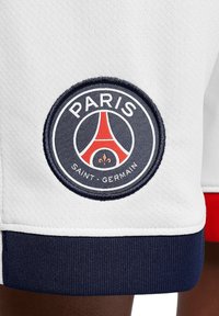 Witte sportshorts met een ronde geborduurde patch met "PARIS SAINT-GERMAIN" en een grafiek van de Eiffeltoren in rode en marineblauwe accenten.