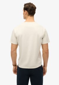 Jasnobeżowa koszulka z krótkim rękawem wykonana z miękkiego materiału. Posiada okrągły dekolt i luźny krój, z delikatnie widoczną fakturą.