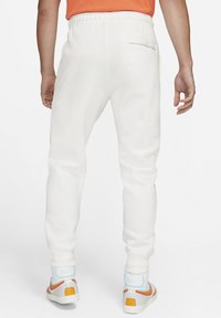 White sweatpants with a tapered fit, elastic waistband, two side pockets, and a back pocket, paired with colorful high-top sneakers.