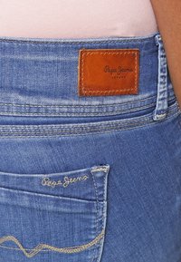 Ljusblå denimjeans med en läderlapp märkt "Pepe Jeans London" och dekorativ sömnad på bakfickan.