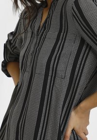 Zwart-wit gestreept shirt met een halve knoopsluiting, lange mouwen opgerold tot de ellebogen en gestructureerde verticale strepen.