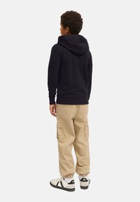 Schwarzer Hoodie mit Kängurutasche, beiger Cargo-Shorts mit Seitentaschen und weißen Sneakers mit schwarzen Akzenten. Die Textur ist glatt, lässige Passform.