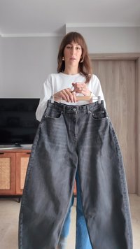 Grå jeans med vida ben och hög midja, med en blekt denimitextur och framfickor, upphängda på en trägalge.