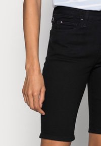 Bermudas de mezclilla negra con diseño ajustado, cintura de altura media y dobladillo con vuelta. Cuenta con bolsillo frontal y detalle sutil de la marca.