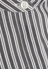 Col de chemise à rayures verticales blanches et noires avec un bouton blanc à quatre trous fermé en haut.