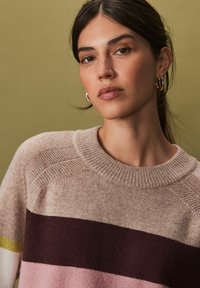 Pull en tricot avec des rayures horizontales beige, bordeaux, rose et jaune, un col rond et un détail texturé aux épaules.