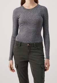 Haut gris à manches longues côtelé avec un col rond, en matériau texturé, associé à un pantalon cargo vert foncé avec des poches et un bouton.
