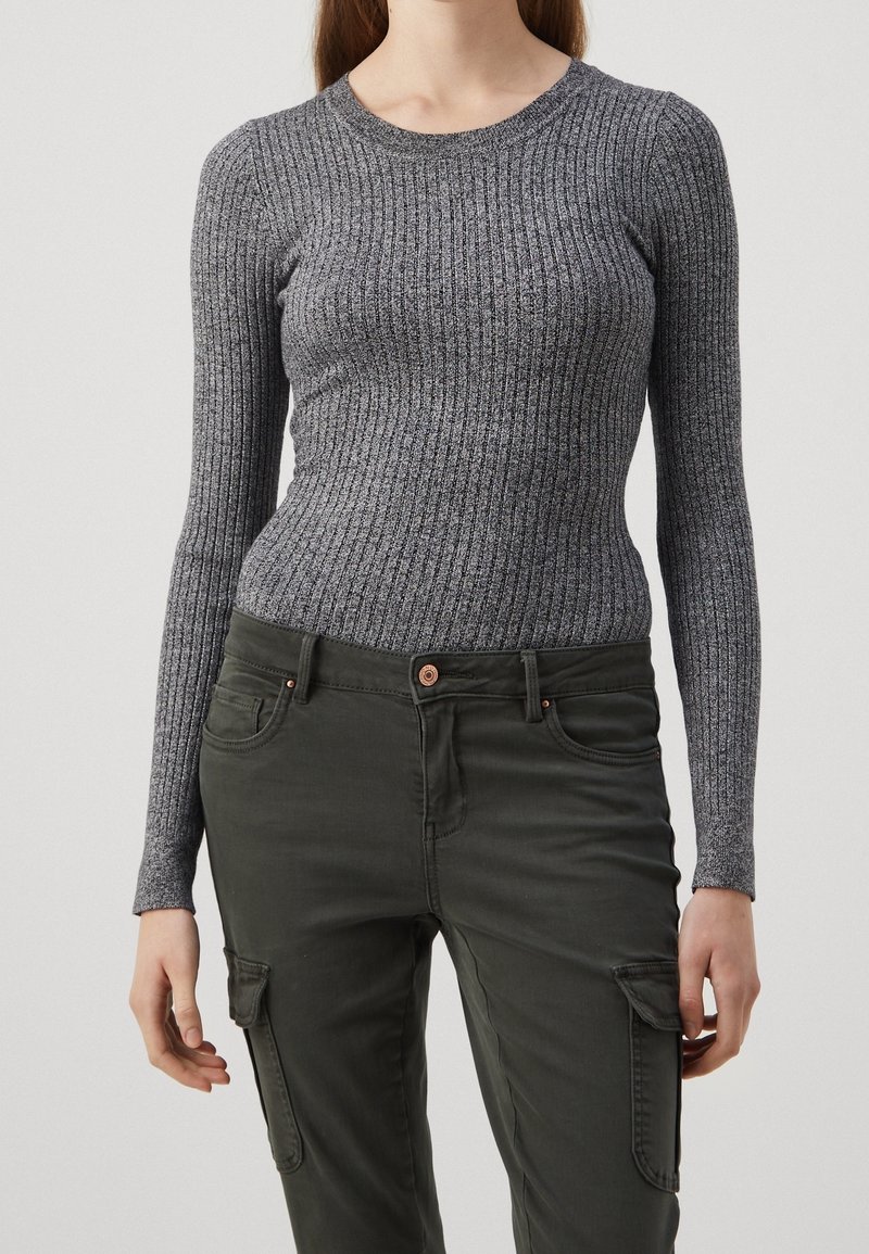 Haut gris à manches longues côtelé avec un col rond, en matériau texturé, associé à un pantalon cargo vert foncé avec des poches et un bouton.