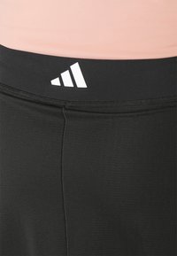 Fekete sportleggings sima, rugalmas anyagból. A derékrészen egy fehér Adidas logó látható.