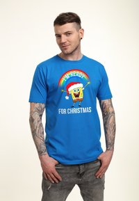 Camiseta de algodón azul con un gráfico de un personaje amarillo sonriente con un gorro de Santa y el texto "ESTOY LISTO PARA LA NAVIDAD" debajo.