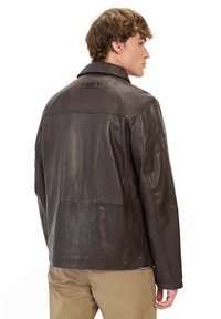 Bruine leren jas met een eenvoudige afwerking, puntige kraag en details op de rug. Bevat zichtbare stiksels en heeft een ontspannen pasvorm.