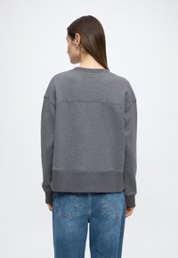 Γκρι φούτερ �από βαμβακερό μείγμα με στρογγυλή λαιμόκοψη, χαμηλωμένοι ώμοι, ριμπ τελειώματα στα μανίκια και κοντό τελείωμα, σε συνδυασμό με μπλε τζιν παντελόνι ψηλόμεσο.