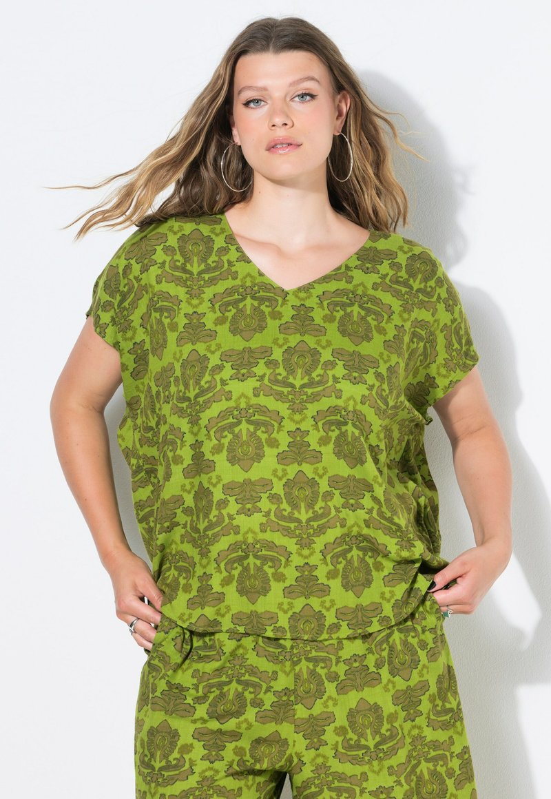 Top verde a maniche corte con scollatura a V e un motivo ornamentale verde scuro. Il tessuto ha un aspetto strutturato, adatto per un abbigliamento casual.