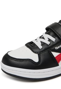 Juodi ir balti sportbačiai su odiniu viršumi, baltais raišteliais, raudonu akcentu, perforuotu pirštu ir lipnia juostele, užtikrinančia saugų prigludimą.