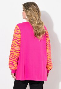 Maglietta a maniche lunghe di colore rosa brillante con maniche a stampa zebra gialla. Realizzata in tessuto morbido, presenta una vestibilità comoda e polsini a costine.