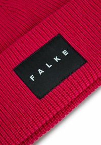 Primo piano di un tessuto lavorato a maglia rosso con un'etichetta rettangolare nera che mostra il nome del marchio "FALKE" in lettere bianche.