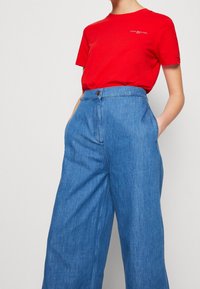 Rød bomulds t-shirt med et lille logo på brystet, parret med brede blå denim bukser med sidelommer og knaplukning.