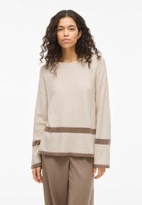 Pull beige à manches longues, col rond, avec des rayures horizontales marron. Texture douce, coupe décontractée, assorti à un pantalon marron coordonné.