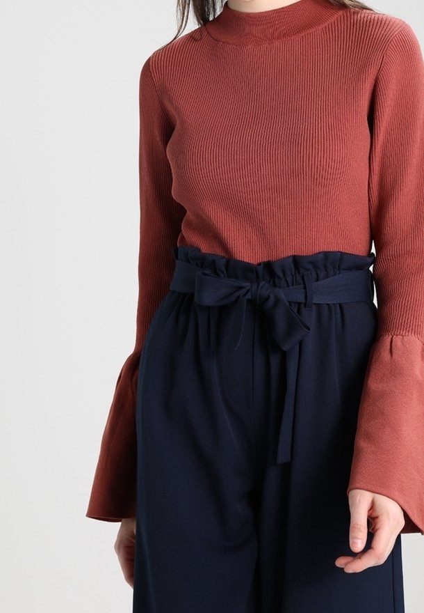 Rostfarbener, gerippter Oberteil mit hohem Kragen und Glockenärmel, kombiniert mit navyblauen, hochtaillierten Hosen mit gebundenem Bund.