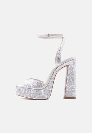 Sandalo platform bianco con tacco alto a blocco, cinturino alla caviglia e decorazioni scintillanti di strass su cinturini e tacco.