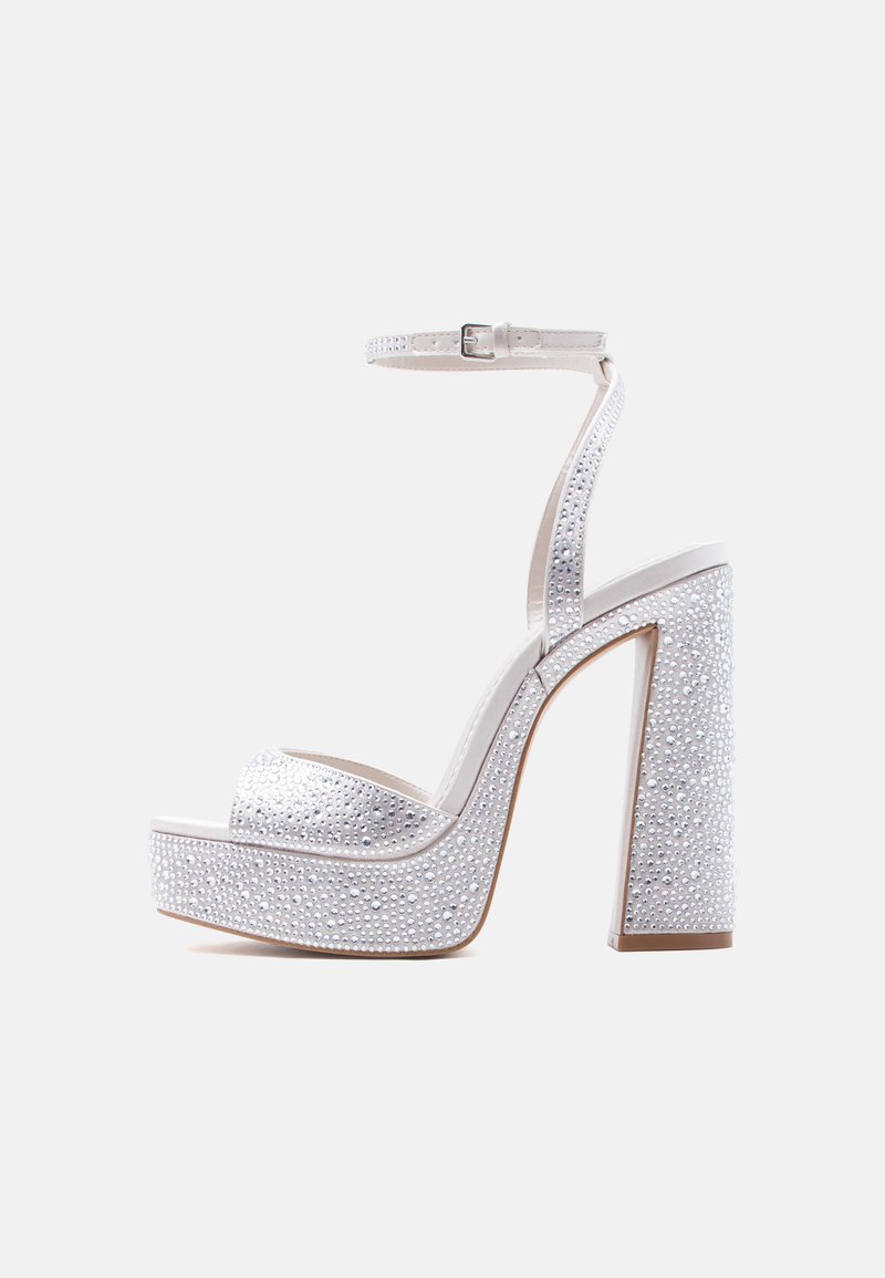 Fehér platformos magassarkú szandál bokapánttal, blokk sarokkal, és csillogó strasszkövekkel díszítve a pántokon és a sarokon.