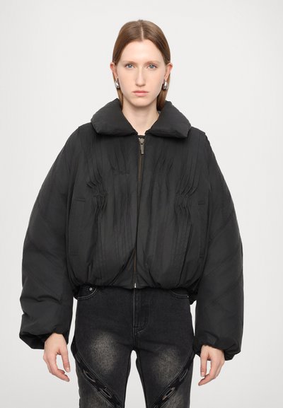 Doudoune noire avec un large col, des plis verticaux sur le devant et une fermeture éclair. Présente des manches amples et volumineuses ainsi qu'une texture lisse.