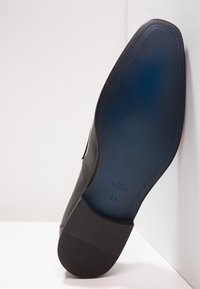 Chaussure habillée en cuir noir inclinée pour montrer la semelle bleue lisse et le talon en caoutchouc avec la taille 42 et "Fatte a Mano" embossé.