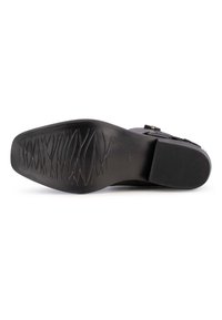 Suela de zapato negra con goma texturizada para agarre, presenta un acabado suave y un diseño de patrón angular. Material duradero, diseñado para la estabilidad.
