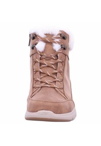 Botte en suède marron à lacets avec bordure en fausse fourrure blanche, dessus texturé et semelle en caoutchouc. Les lacets présentent un motif en zigzag blanc.