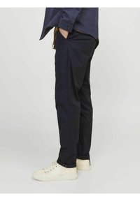 Pantaloni chino blu navy realizzati in misto cotone, con una vestibilità dritta, tasche laterali e risvolti. Abbinati a sneaker beige.