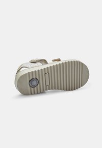 Kultavuoratut sandaalit beige kumipohjalla, jossa on uurteinen rakenne ja joustava muotoilu. Mukana säädettävät hihnahardware.