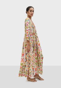 Lång, flerlagers maxi klänning i ett livligt, flerfärgat mönster med blommönster och geometriska design, med långa ärmar och V-halsringning.