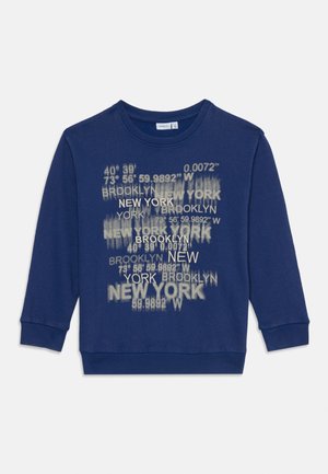 Blå genser med rund hals, med et grafisk trykk av New York- og Brooklyn-koordinater i hvit og lys grå. Myk bomullsblanding.