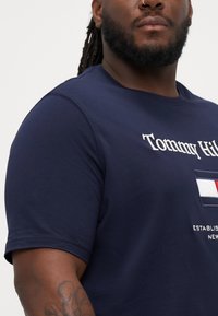 Marine bomull T-skjorte med logo trykk, rund hals og korte ermer. Merkbare detaljer inkluderer brodert merkevare og en fargeblokkert lapp.