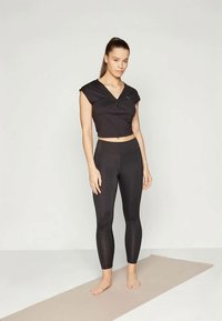 Black cropped sports top with a knot detail, paired with high-waisted black leggings. Smooth texture, form-fitting design suitable for workouts.