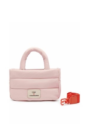Bolso acolchado de color rosa suave con asas redondeadas y parche rectangular blanco con el logo, acompañado de una correa extraíble de color rojo brillante con ganchos.
