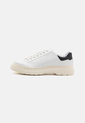 Weiße Leder-Sneaker mit strukturierter Oberfläche, kontrastierendem schwarzen Fersenelement, runder Zehenpartie und dicker beige Gummisohle. Verfügt über Schnürsenkel und ein Logo.