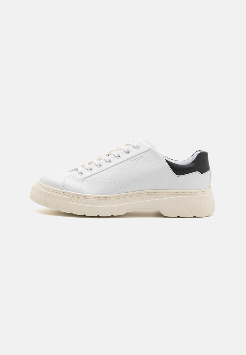 Hvite lær sneakers med teksturert overflate, kontrastfarget svart hæl, rund tå og tykk beige gummi såle. Har snøring og logo.