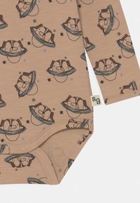 Bodysuit bege de mangas longas com um padrão repetido de cães de desenho animado em anéis e estrelas. Feito de tecido suave com fecho de pressão na parte inferior.