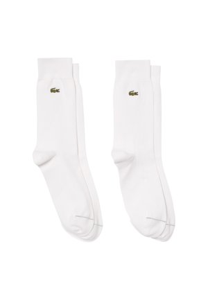 Chaussettes en coton blanches avec des bords côtelés, arborant un petit logo crocodile vert de Lacoste sur le côté extérieur. Texture douce et design classique.