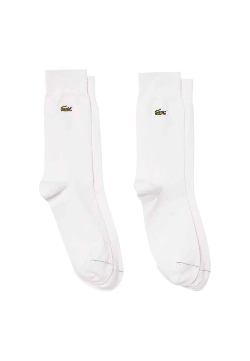 Weiße Baumwollsocken mit geripptem Bündchen, versehen mit einem kleinen grünen Lacoste-Krokodil-Logo auf der Außenseite. Glatte Textur und klassisches Design.