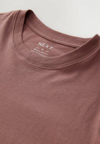 Camiseta de cuello redondo de manga corta en color marrón, hecha de una tela suave, con una etiqueta visible que muestra el nombre de la marca "NEXT" y el tamaño "M".