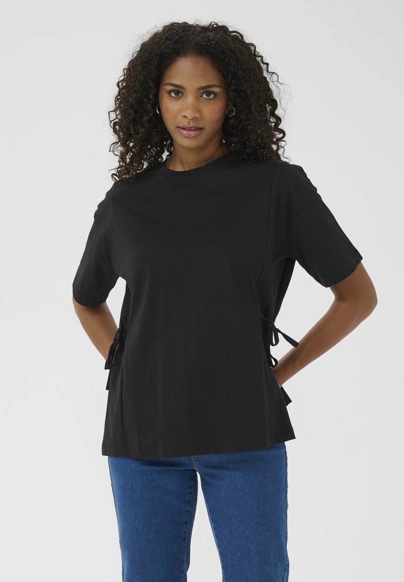 Black short-sleeve t-shirt with side ties, crafted from smooth cotton. Features a relaxed fit and crew neckline. Paired with blue jeans.