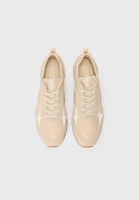 Beige treningssko med nettingpaneler, teksturerte detaljer og snøring. Har gummisåle og diskret merkevarebygging på tungen.
