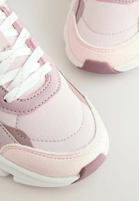 Pantofi sport roz, cu un amestec de materiale netede și texturate, șireți albi și o talpă groasă albă cu accente lavandă.