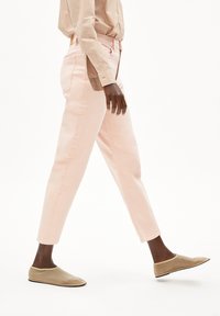 Pantalon droit rose clair en coton, avec un design classique à cinq poches et un minimum de détails, assorti de chaussures de type slip-on beiges.