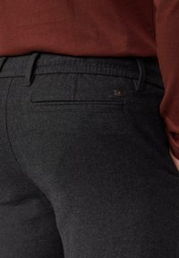 Donkere grijze broek van gestructureerde stof, met een achterzak met een subtiel metalen accent en een gladde tailleband.