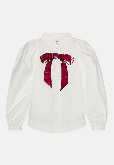 White button-up shirt with puffed sleeves, featuring a red sequin bow design on the front and a classic collar. Smooth fabric texture.