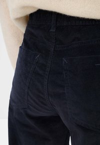 Navy corduroy pants featuring a textured surface, two back pockets, and a high waist. A light beige top is partially visible.