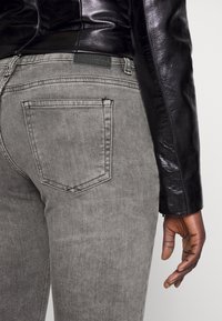 Jeans de mezclilla gris con un bolsillo trasero, combinados con una chaqueta de cuero negro brillante. La tela tiene una textura suave.